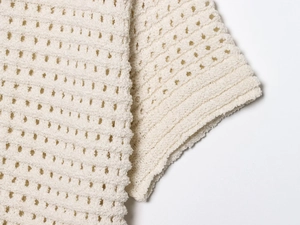 Macro detail of cream knit fabric with fringe fringe edges and delicate hollow-out pattern