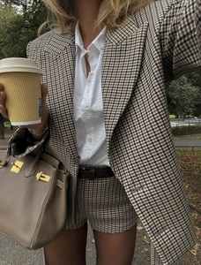 Close-up of brown plaid blazer fabric with leather belt and classic handbag details