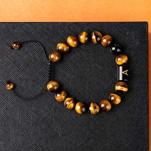 Macro detail of natural tiger eye stone beads and black letter A charm on woven bracelet