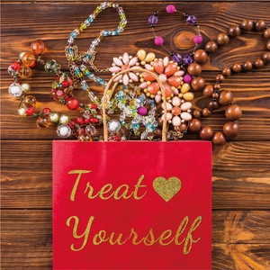 Variety of handmade necklaces with floral charms and beads next to a Treat Yourself gift bag