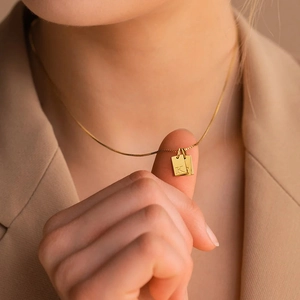 Detailed view of a gold double rectangular pendant necklace with engraved letter K on a model