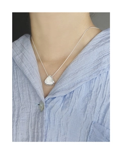 Detail of a silver shell pendant necklace on a model wearing a light blue shirt