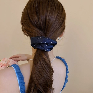 Detail of a navy blue satin polka dot scrunchie worn on a high ponytail style