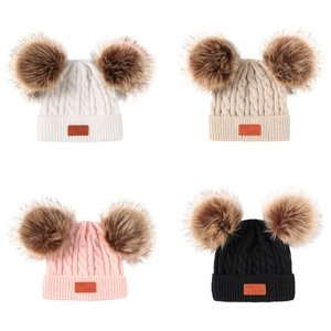 Detailed view of four cable-knit winter hats in white, beige, pink and black with double pom-poms