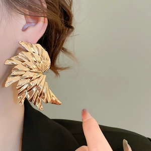 Detailed close-up of a golden pleated fan-shaped earring worn on a fashion model