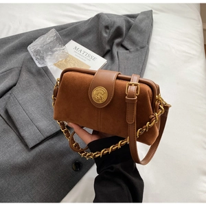 Detail of a brown frosted leather doctor bag featuring a vintage metal emblem and gold chain