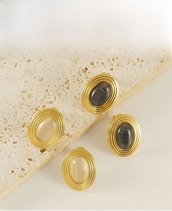 Vue détaillée des boucles d'oreilles ovales en acier avec bord texturé et pierres œil-de-chat