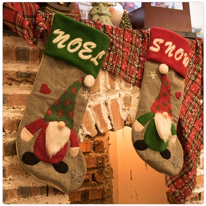 Detail of knitted Christmas stockings with faceless gnomes hanging on a fireplace