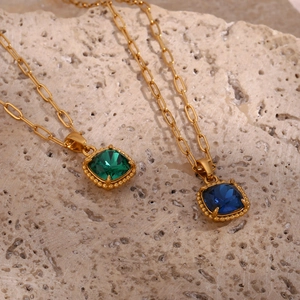 Detail view of emerald and sapphire pendant necklaces on paperclip chain over natural stone