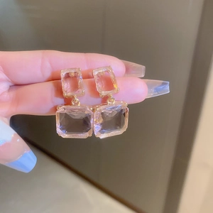 Detail view of pink crystal square earrings with gold plating held in hand