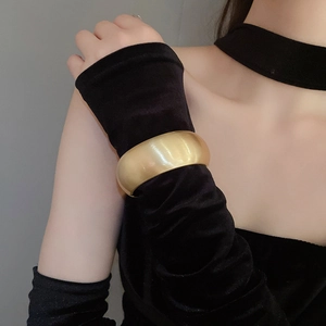 Detail of wide matte gold open bangle over a black velvet sleeve showing high-end texture