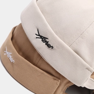 Detail of embroidered Aster text on stacked beige and khaki cotton docker caps