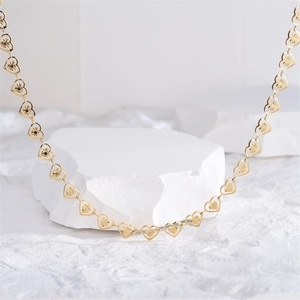 Minimalist gold heart chain necklace with engraved hollow heart links on white stone