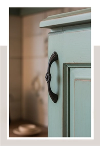 Close-up of vintage cast iron drawer handle with embossed floral pattern on mint green wood