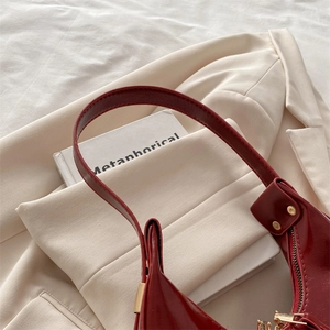 Fashionable dark red patent leather shoulder bag with gold hardware on white blazer