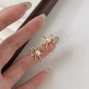 Close-up of small bow-shaped pearl stud earrings held on a fingertip for size scale