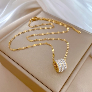 Macro detail of gold cylinder pendant with paved white crystals on delicate chain