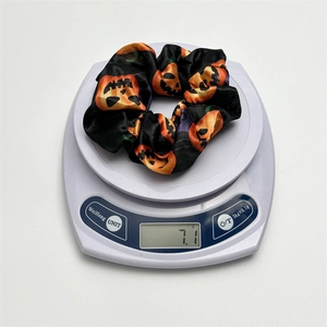 Halloween black satin scrunchie with orange pumpkin patterns displayed on a digital scale