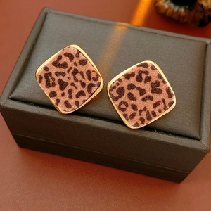 Détail de boucles d'oreilles carrées léopard avec bordure dorée sur cuir noir