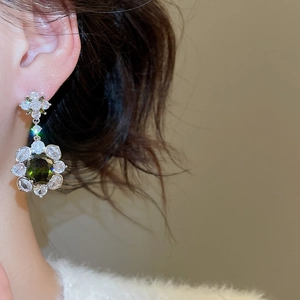 Macro detail of silver flower earring with emerald green stone worn by a model