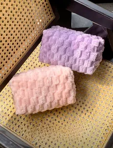 Detailed close-up of cloud pleated plush makeup bags in purple and pink on a rattan surface