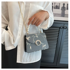 Close-up of floral embroidery detail and elegant pearl handle on a small square crossbody bag
