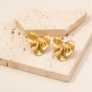 Macro view of golden 18k plated irregular pleated heart stud earrings with mirror finish