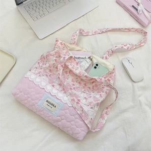 Detail of pink floral quilted tote bag with lace trim and heart stitching on a bed