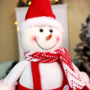 Plush Christmas snowman doll with red knitted hat and scarf in warm festive background