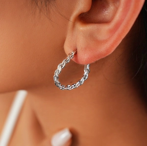 Gros plan d'une créole torsadée en argent portée à l'oreille avec texture tressée