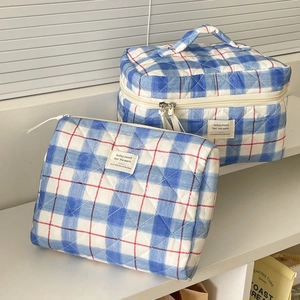 Close-up of quilted blue plaid toiletry bag set with red zipper detail on white steps