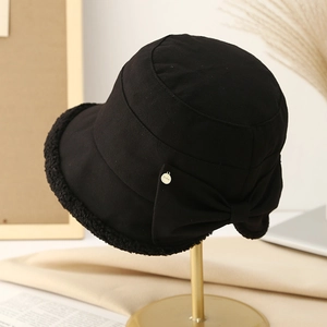 Minimalist black winter bucket hat with bow detail and plush trim on a display stand
