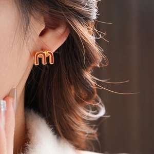 Macro shot of gold double-arch letter earrings with red enamel on a model side view