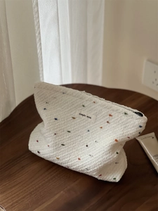Detailed texture of white knit makeup bag featuring colorful dots and simple wish label