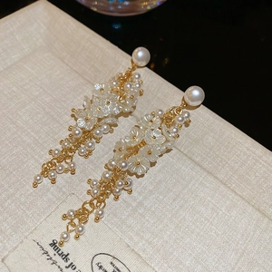 Detail of floral tassel earrings with white pearls and gold chains on a textured surface