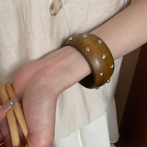 Gros plan d'un large bracelet en bois avec rivets argentés porté sur une manche beige