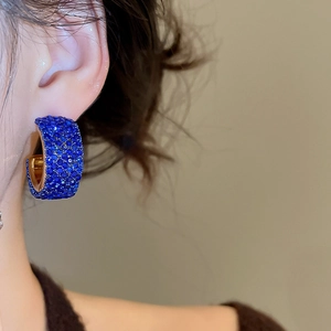 Detailed view of wide C-shaped gold hoop earrings with pavé-set blue crystals