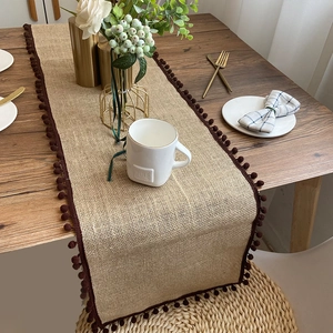 Bohemian jute table runner with dark brown pom-pom edges on a rustic wooden dining table