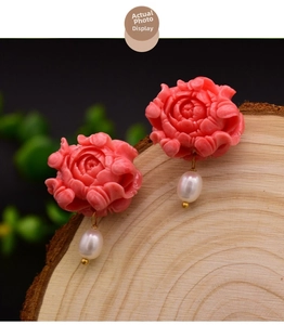 Detail of pink carved floral earrings with white drop-shaped natural pearls and silver studs