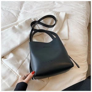 Close-up of black leather bucket bag featuring MACGHEE logo on beige suit jacket