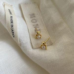 Close-up of golden bear-shaped pearl stud earrings on a textured linen background