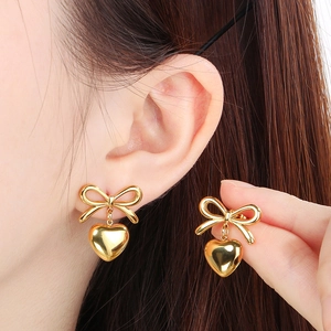 Close-up of 18k gold ribbon bow and heart earrings worn by a model for a sweet style