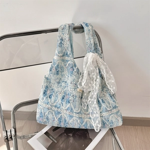 Macro view of blue fabric shoulder bag featuring white lace floral embroidery and bow