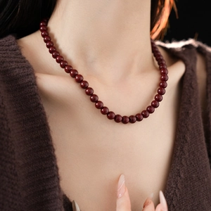 Close-up of a minimalist deep red beaded necklace worn by a model in soft lighting