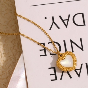 Macro view of gold-plated heart pendant with white pearl shell inlay on a white card