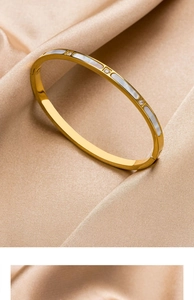 Detail eines Armreifs aus Gold-Titanstahl mit weißer Muschel und funkelnden Kristallen