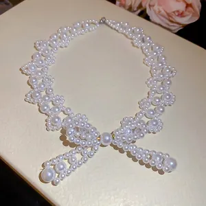 Elegant stainless steel bow pearl necklace on a textured beige gift box with pink flowers