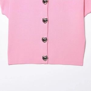 Pink knit short sleeve top featuring decorative silver heart buckles in a flat lay view