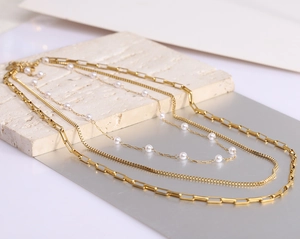 Detail of triple-layer 18K gold-plated chain necklace with elegant white pearls on stone