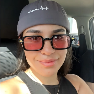 Close-up of retro square black sunglasses with pink lenses worn with a grey knit beanie